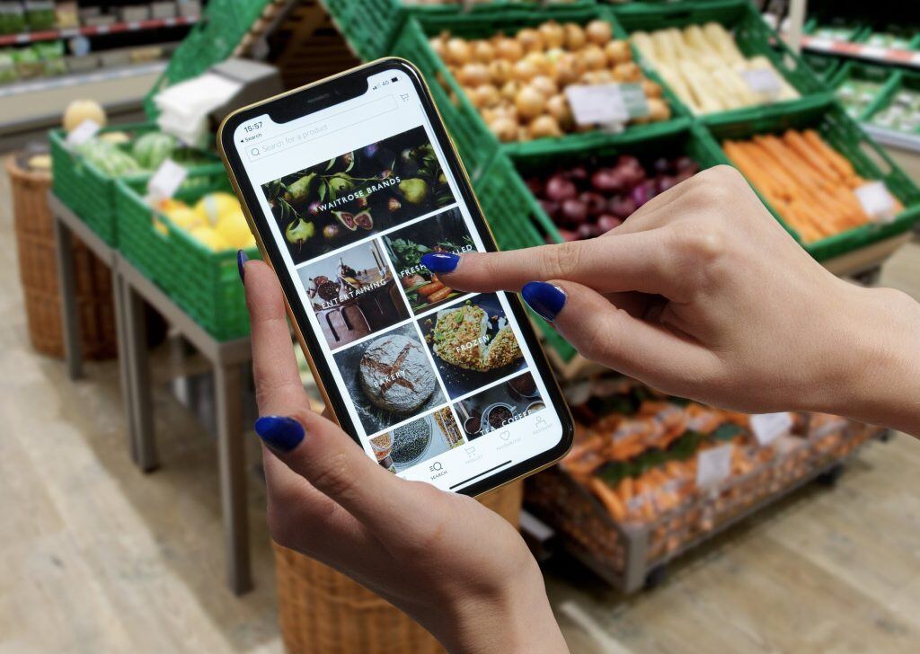 A person with blue nail polish uses a smartphone to browse recipes while in a grocery store produce section.